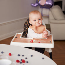 Ladda upp bild till gallerivisning, Ett barn som sitter i en barnstol och äter frukt och grädde ,med haklapp på