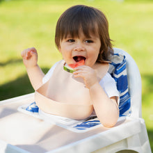 Ladda upp bild till gallerivisning, Ett barn som äter vattenmelon och har haklapp och sitter i en barnstol